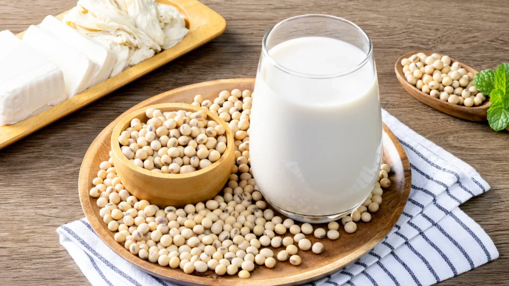 Le lait de soja fait partie des boissons végétales issues de cette légumineuse Verre de lait de soja entouré de graines de soja et de morceaux de tofu.